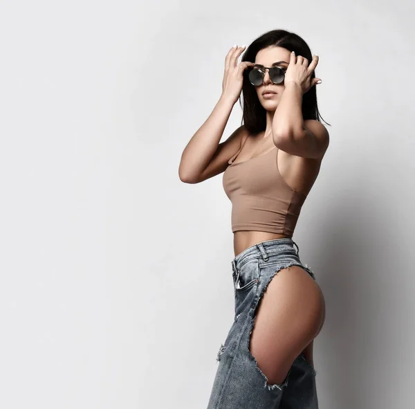 Self-confident sexy adult woman is walking in torn jeans with naked butt, ass, sunglasses and top. Side view — Zdjęcie stockowe