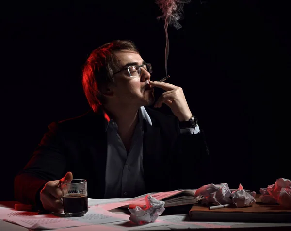 Homem adulto de camisa e casaco senta-se atrás da mesa, escrevendo mesa com livro e papéis, bebe chá, café e fuma — Fotografia de Stock