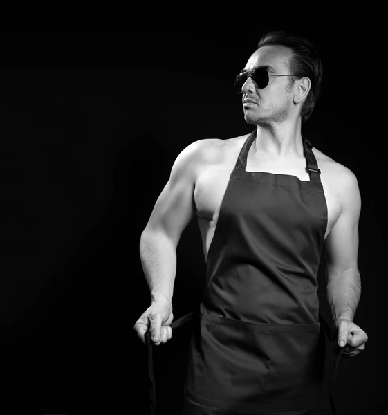 Schwarz-Weiß-Porträt eines ruhigen, selbstbewussten, muskulösen, erwachsenen Mannes mit Sonnenbrille und Schürze auf nacktem Körper — Stockfoto
