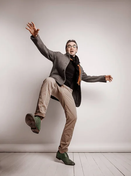 Adult man in pants and plaid jacket stands holding foot up, making giant step, falling down waving hands