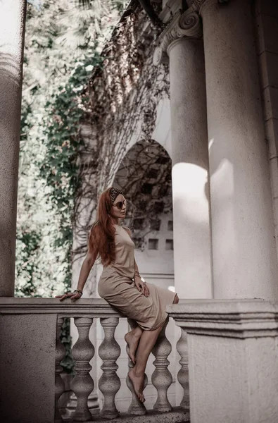 Junge Touristin im Sommerkleid sitzt auf der alten Balustrade der alten Palastterrasse und betrachtet die klassische Säule — Stockfoto
