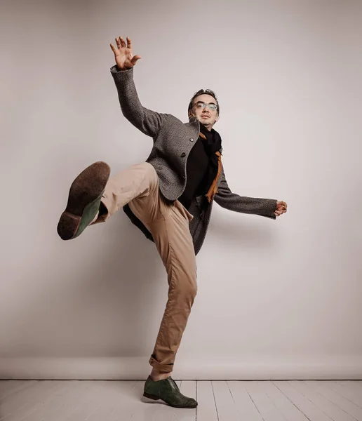 Homem adulto elegante hipster em calças e jaqueta xadrez fica segurando pé para cima, fazendo passo gigante, caindo mãos onduladas — Fotografia de Stock