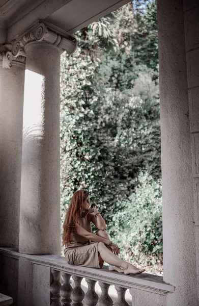 Junge Touristin im Sommerkleid sitzt mit nackten Füßen auf der alten Balustrade der alten Palastterrasse, Pavillon — Stockfoto