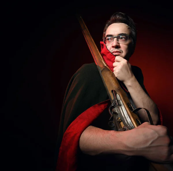 Soldier of past times standing sideways with his rifle slung over his shoulder, holding collar of cape and looking back — Foto Stock