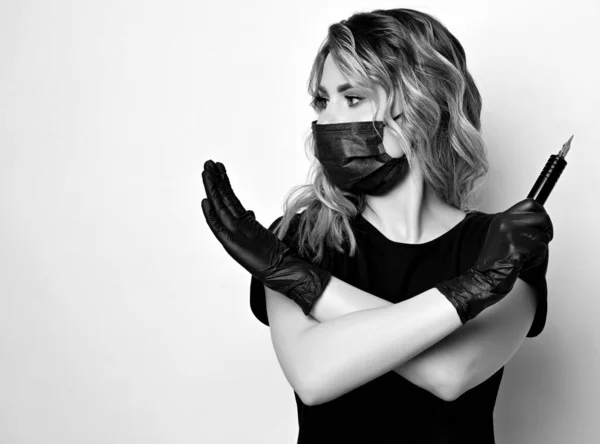 Zwart op wit. Curly vrouw in beschermende medische masker en handschoenen met permanente make-up machine in de hand gebaren kruis — Stockfoto