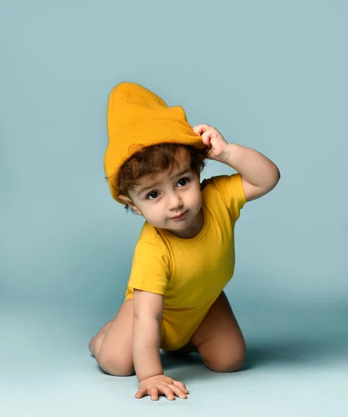 Pequeño lindo sonriente rizado bebé niño en amarillo cómodo mono y sombrero arrastrándose en el suelo —  Fotos de Stock