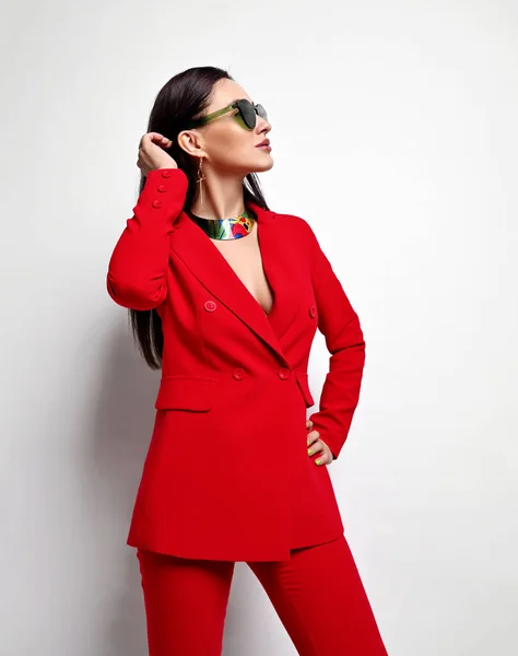 Portrét mladé arogantní brunetky podnikatelky v červených oficiálních kalhotách a slunečních brýlích stojící stranou — Stock fotografie