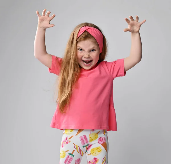 穿着粉色T恤和五颜六色裤子的活泼、嬉闹的红头发小女孩牵着手和爪子玩耍野兽 — 图库照片