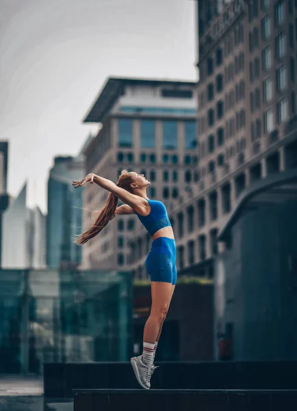 Jonge sportieve vrouw in de zomer sportkleding shorts en top staat zijdelings op tenen, zweven op straat in Dubai Stockafbeelding