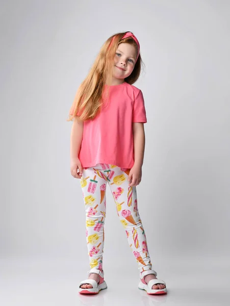 红头发的小女孩，穿着夏装，穿着粉色T恤，色彩艳丽的裤子，上面印着雪糕和凉鞋 — 图库照片