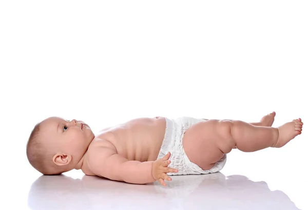 Baby kind meisje meisje kind in luier ligt op haar rug zijwaarts naar camera, kijken omhoog en houden haar benen omhoog — Stockfoto