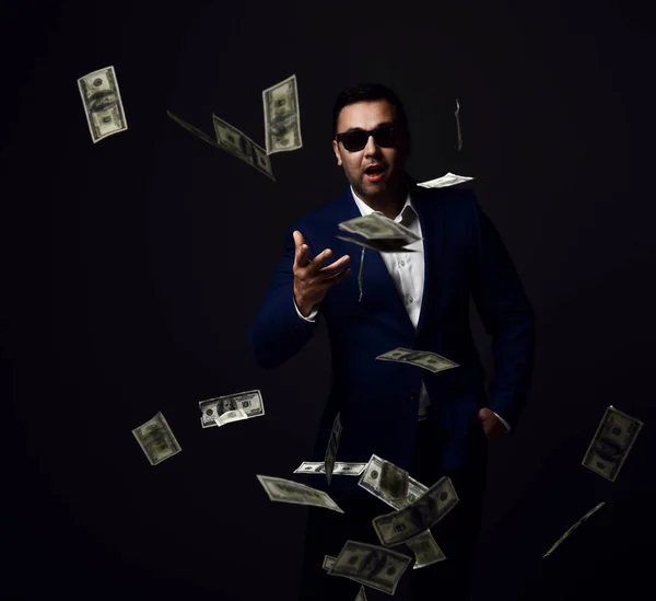 Retrato de rico empresário de sucesso em casaco azul e óculos de sol de pé jogando dólares em dinheiro na câmera — Fotografia de Stock