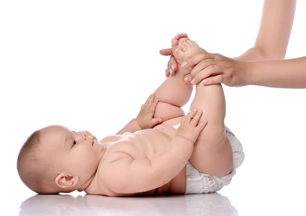 Bebé bebé niña en pañal está acostada boca arriba tocando sus rodillas mientras hace ejercicios para fortalecer los músculos —  Fotos de Stock