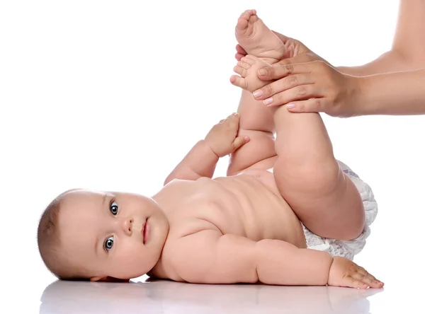 Infant baby girl kid in diaper is lying on her back doing exercises, bending knees with adult coach, mother. Side view — Stock Photo, Image