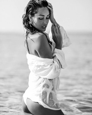 Sexy young woman with perfect buttocks in bikini and shirt stands in clear sea water. Black and white. Summer vibes
