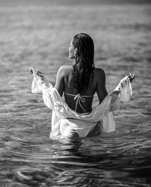 Сексуальная женщина в белом бикини и рубашке уходит глубже в чистую морскую воду. Черное и белое. Летние вибрации — стоковое фото