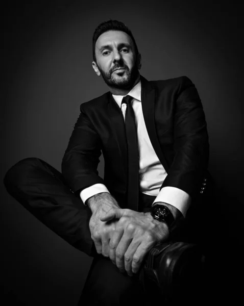 Чорно-білий. самовпевнений, потужний бізнесмен в сучасному офісному костюмі сидить з перехрещеними ногами, тримаючи ногу — стокове фото