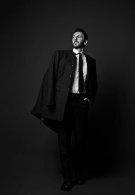 Siyah ve beyaz. Zengin, göz kamaştırıcı iş adamı, modern ofis kıyafeti giymiş patron omuzlarında ceketini duruyor ve yan bakıyor.