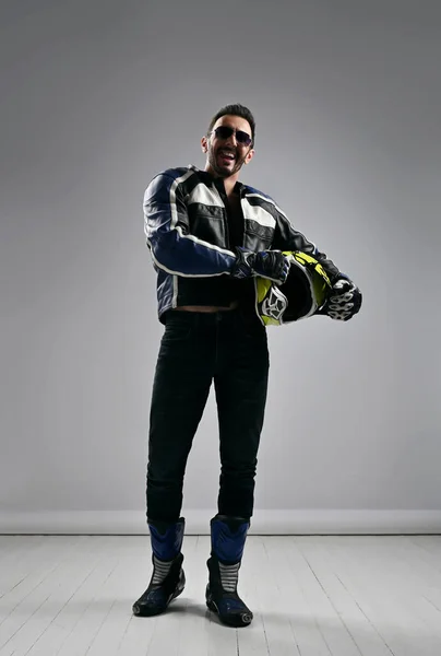 Ευτυχισμένος αξύριστος ενήλικας ποδηλάτης motocross racer σε μπότες δερμάτινα γρανάζια μοτοσικλέτας, σακάκι και γάντια βόλτες με το κράνος του — Φωτογραφία Αρχείου
