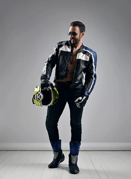 Brutale unrasierte erwachsene Mann Biker Motocross-Rennfahrer in Motorrad-Ausrüstung Stiefel, Jacke und Handschuhe geht mit Helm in der Hand — Stockfoto