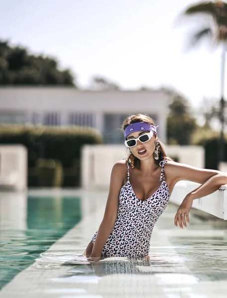 Jonge sexy vrouw in witte luipaard print bikini staat sexy poseren in het zwembad op hotel site tijdens vakantie — Stockfoto