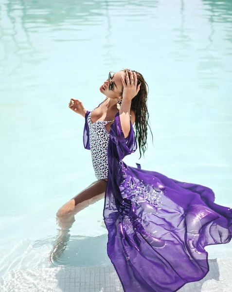 Sexy Frau mit großer Brust im Bikini mit weißem Leopardenmuster und lila Pareo steht seitlich im Pool und berührt ihr nasses Haar — Stockfoto