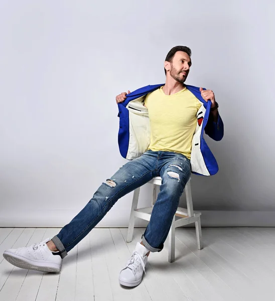 Hombre adulto sin afeitar en jeans rasgados, camiseta amarilla se sienta en el taburete con su chaqueta azul abierta, mostrando que no tenía nada — Foto de Stock