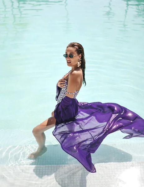 Rijk sexy vrouw met grote borst in witte luipaard print bikini en paarse pareo staat zijdelings in het zwembad tijdens vakantie — Stockfoto