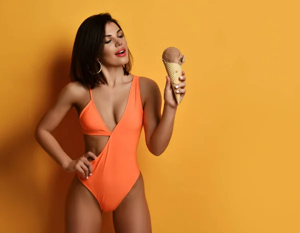 Portakallı bikinili, gülümseyen seksi bayan elinde çikolatalı dondurmayla ayakta duruyor. — Stok fotoğraf