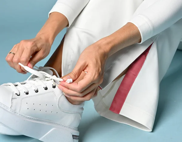 Closeup of woman hands ties shoelaces of her fashionable white sneakers