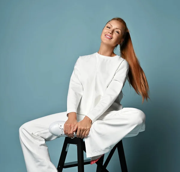 Mulher nova na moda feliz com penteado de rabo de cavalo em pantsuit casual na moda branca, estilo quimono senta-se na cadeira — Fotografia de Stock