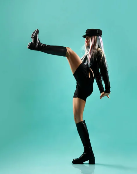 Молода блондинка з кольоровими нитками в чорній шкірі сексуальний костюм і високі черевики стоять і роблять удар ногою — стокове фото