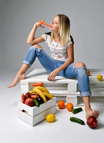 Женщина ест морковь возле коробки со свежими органическими овощами и f — стоковое фото