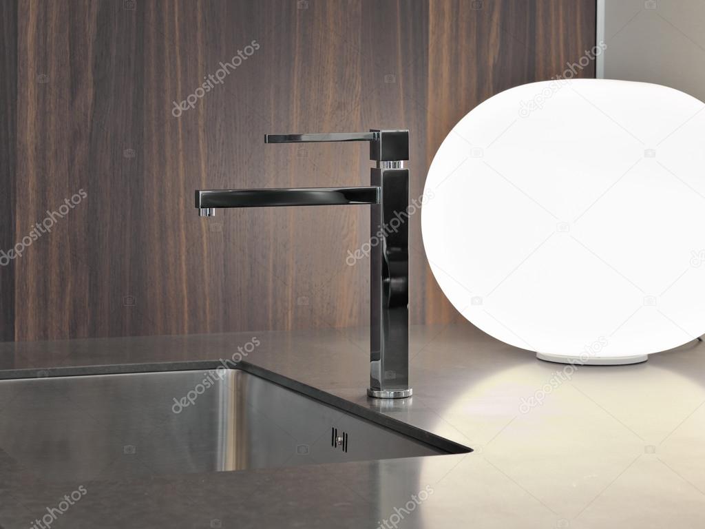 Detail of steel faucet in modern kitchen near to lamp