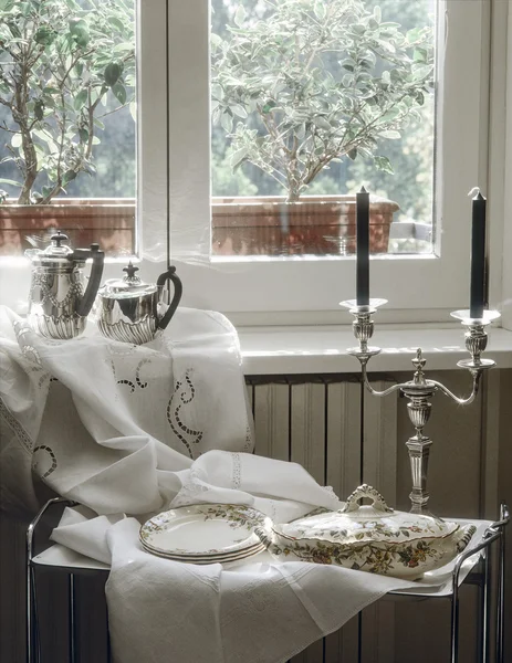 Ancient sauce boat, soup tureen and candelsticks near to window — Stock Photo, Image