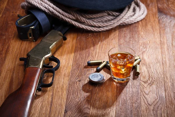 Old west rifle and ammunitions with glass of whisky and ice with old silver dollars coins on wooden bar table