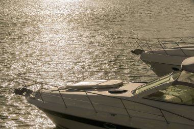 Güneşin altında denize demirlemiş yatlar, arka planda birbirine yakın deniz araçlarının parçaları.