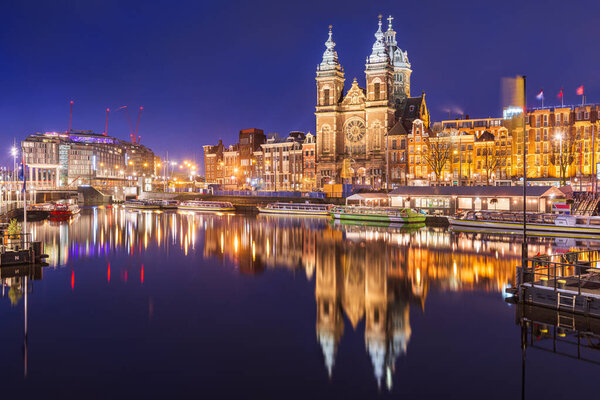 Amsterdam, Netherlands city center view with riverboats and the  Basilica of Saint Nicholas at night.