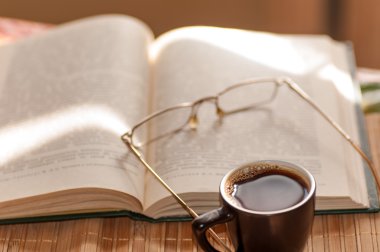 Fincan kahve, açık kitap ve gözlük