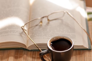 Fincan kahve, açık kitap ve gözlük