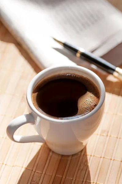 Cup of black coffee, newspaper and a pen — Stock Photo, Image