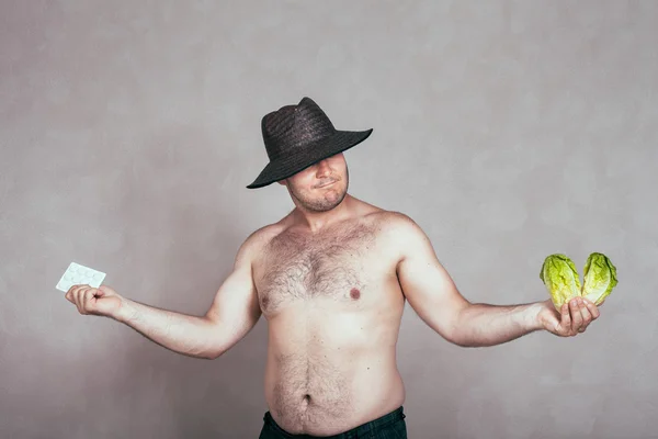 Indecisive naked corpulent man with pharmaceuticals and vegetable — Stock Photo, Image