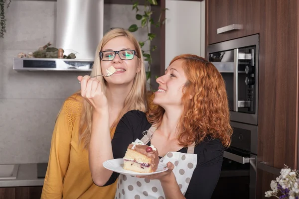 Feliz namoradas comer bolo na cozinha — Fotografia de Stock