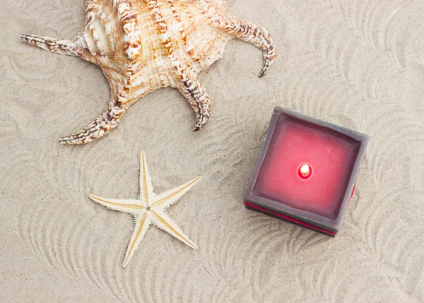 Seashells e uma vela de lit em uma praia de areia — Fotografia de Stock