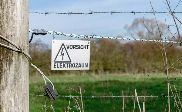 A German warning caution sign hanging on an electrified electric fence in the countryside
