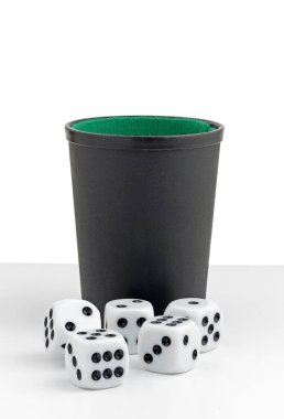 Beyaz arka planda yeşil keçeli kalemle siyah bir bardağın önünde yatan beş beyaz zar.