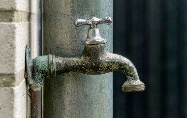 Yıpranmış bir bahçe musluğunun yakınında hortum için vida teli takılı bir musluk.