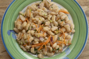 Ev yapımı cannellini fasulye salatası, doğranmış havuç, soğan ve yeşil dekoratif tabakta taze maydanoz, sağlıklı Akdeniz mezesi veya hafif yemek.