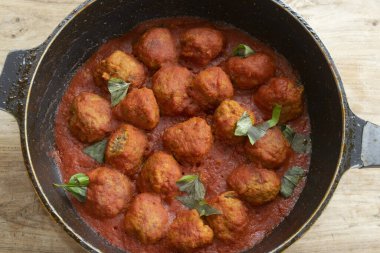 Zengin domates sosunda kaynayan ev yapımı İtalyan köfteleri ve siyah yaprak dökme demir tavada taze fesleğen, yukarıdan geleneksel konforlu yemek tarifi.