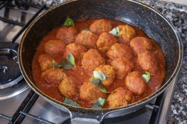 Ev yapımı köfteler, geleneksel İtalyan yemeği hazırlamak için fırında taze fesleğen yapraklı domates sosunda kaynıyor.